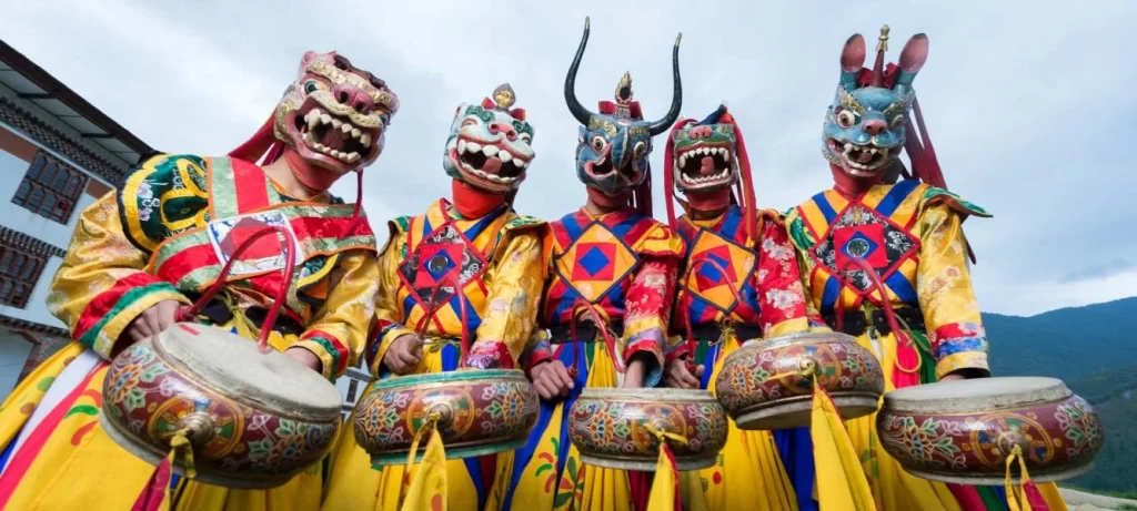 Bhutan travel etiquette: masked dancers with drums perform a traditional cultural dance in colorful costumes. About Bhutan.