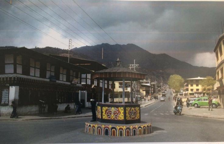 Bhutan in the 90s: Street scene with traditional architecture, cars, and mountain backdrop.