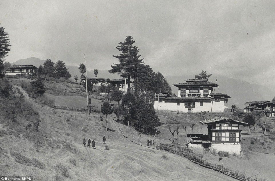 Bhutan circa 1900s: Black and white image of traditional Bhutanese buildings dotting a hillside landscape, historic architecture.